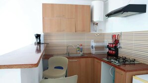 A compact kitchen with wooden cabinets, a gas stove, a sink, and a chair.