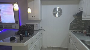 A kitchen with white cabinets, a microwave, a clock, and a TV displaying a message. - 3-bedroom townhome in beautiful Puerto Peñasco with AC blocks from beach. (Puerto Peñasco)