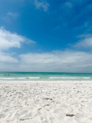 Een strand met wit zand en turquoise water onder een helderblauwe lucht.