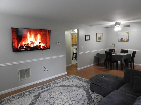 A living room with a fireplace, a dining area, and a ceiling fan.