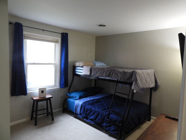 A bunk bed room with a desk and chair, a window with curtains, and a ceiling light.