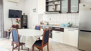 Ett kompakt kök med en matplats, med ett kaklat stänkskydd, ett kylskåp i rostfritt stål och en platt-TV som är monterad på väggen.