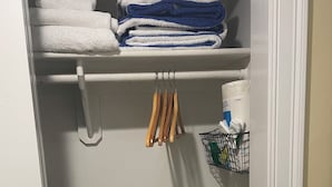 A closet with neatly folded towels, a hanging rack with wooden handles, and a plastic-wrapped item on the bottom shelf. -  Awesome Ocean Front Vacation Condo on the Cape in MA (Dennis)