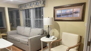 A living room with a grey sofa, a white armchair, a small round table with a lamp, and a framed picture on the wall. -  Awesome Ocean Front Vacation Condo on the Cape in MA (Dennis)