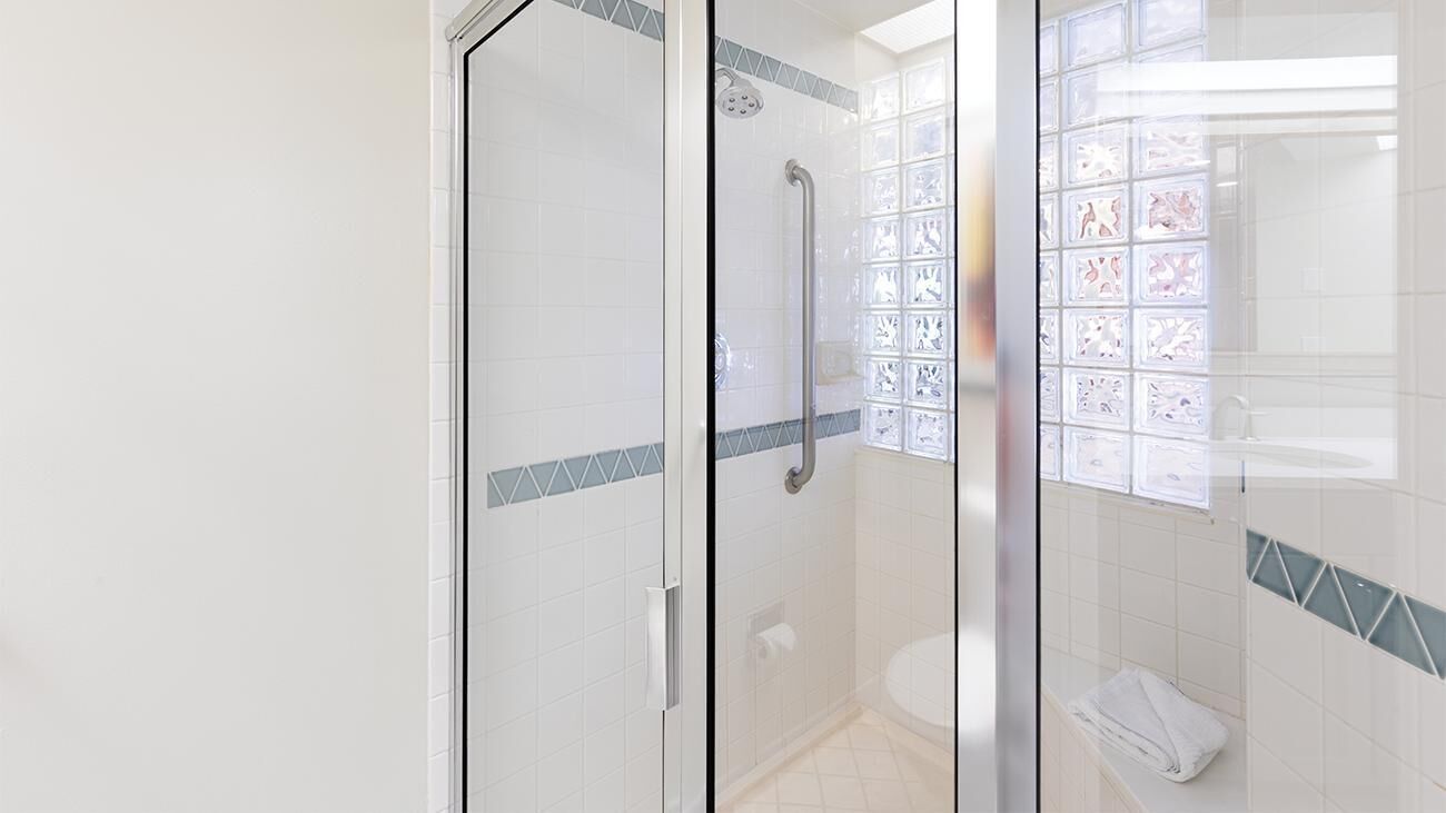 Een douche met glazen wand, een handgreep, witte betegelde wanden en een klein handdoekenrek.