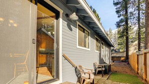 Una casa con puerta corrediza de vidrio, un patio con mesa y sillas, y una terraza de madera.