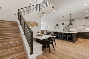 Una cocina moderna con una isla central, taburetes de bar y una escalera con barandilla.