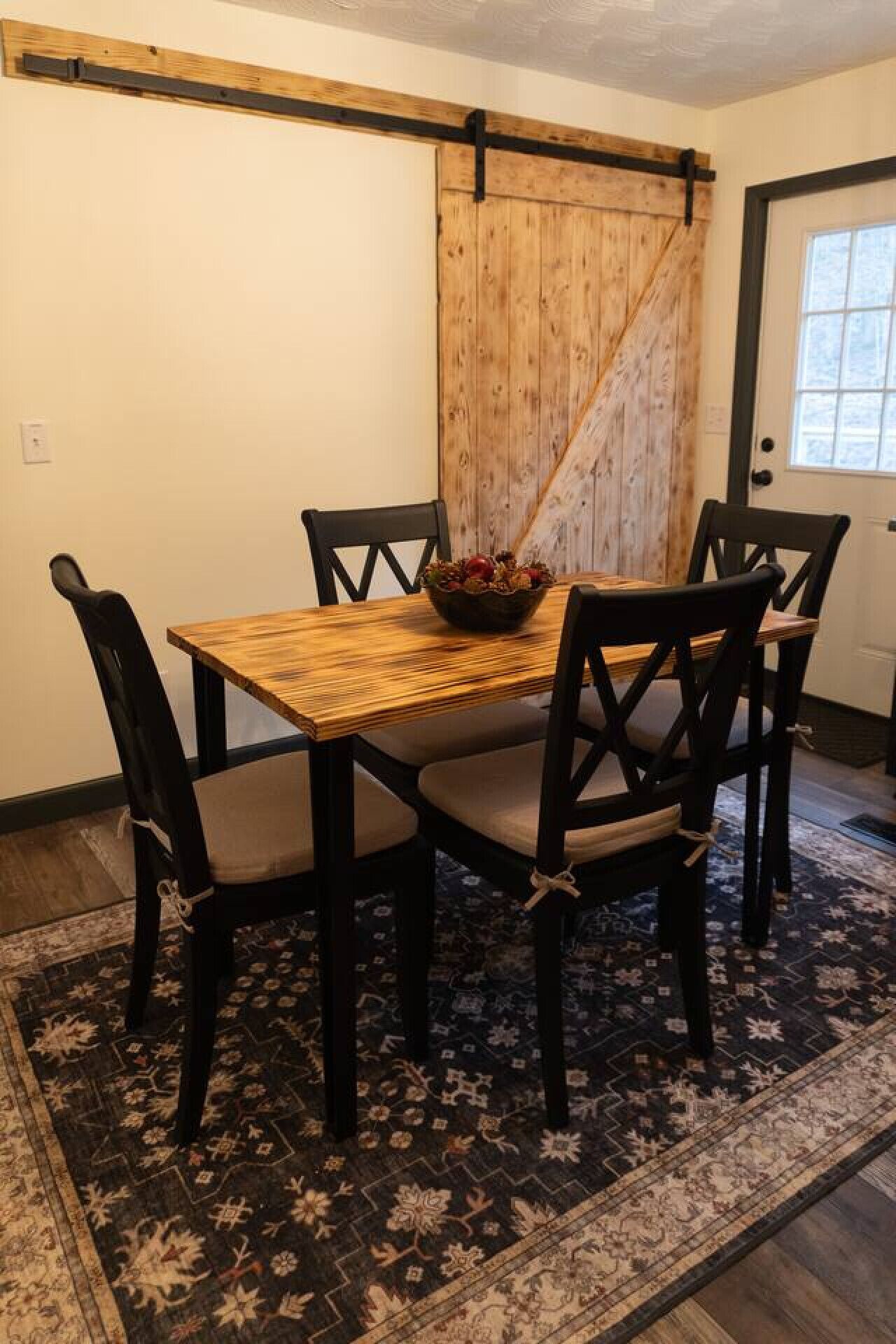A dining area with a wooden table and chairs, a rustic barn door, and a patterned rug.