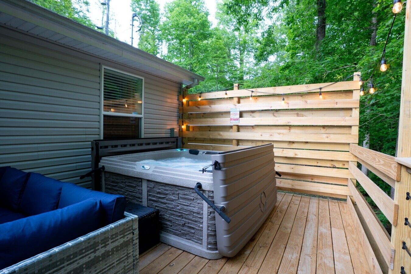 Un jacuzzi en una terraza de madera con cerco de madera y luces colgantes.