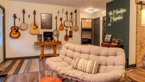A cozy living room with a cushioned sofa, a wooden coffee table, and a variety of string instruments hanging on the wall. - The Mountain Magnolia *Hot tub on private deck* (Inez)