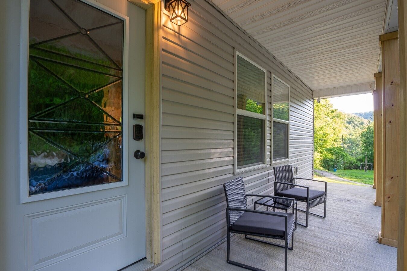 A covered porch with a door, a window with a view, and two chairs.