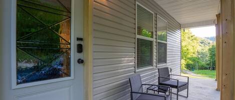 A covered porch with a door, a window with a view, and two chairs.