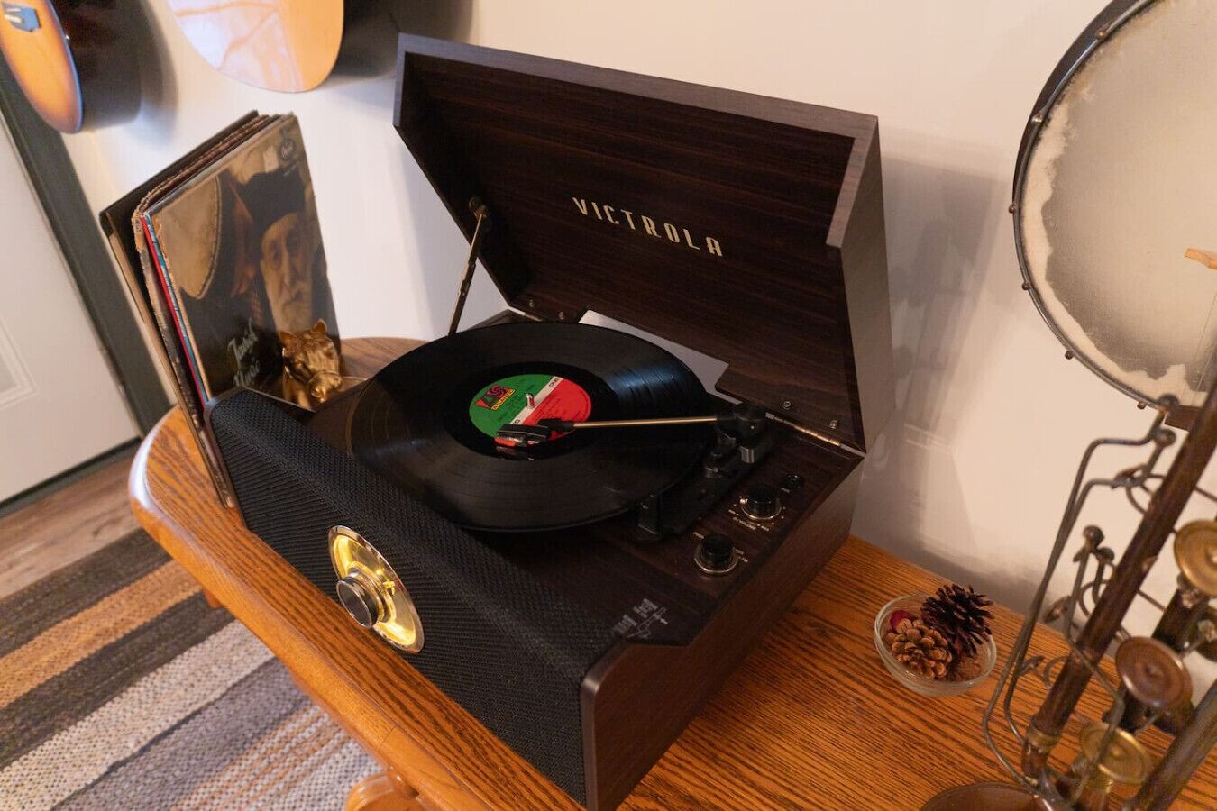 Een houten muziekspeler met een vinylplaat, een schaaltje noten en een kat op de achtergrond.