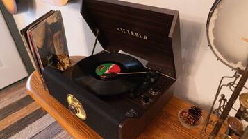Een houten muziekspeler met een vinylplaat, een schaaltje noten en een kat op de achtergrond.