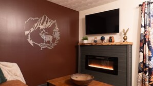 A living room with a fireplace, a mounted TV, and a decorative wall piece. - The Mountain Magnolia *Hot tub on private deck* (Inez)