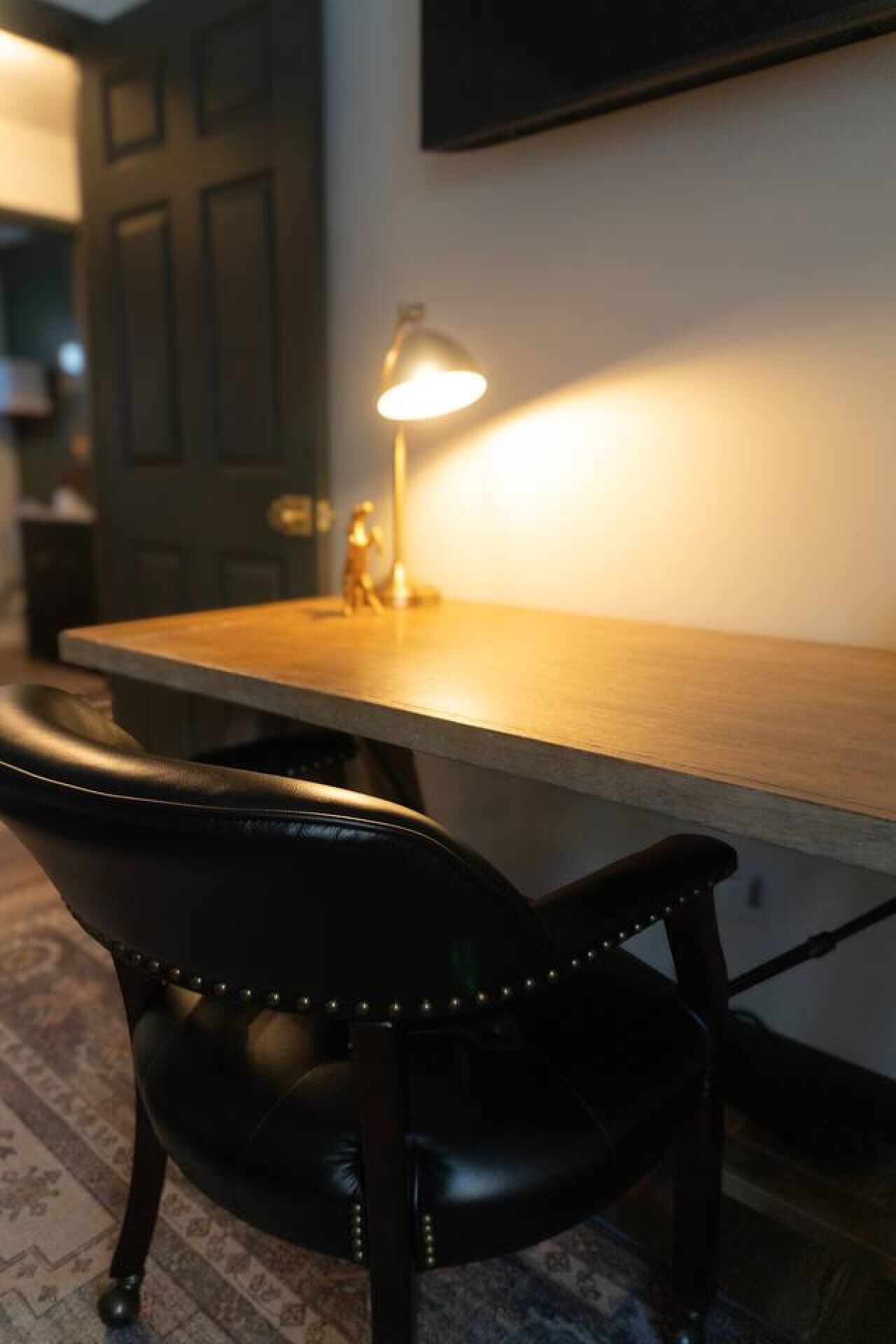 A desk with a lamp, a chair, and a door in the background.