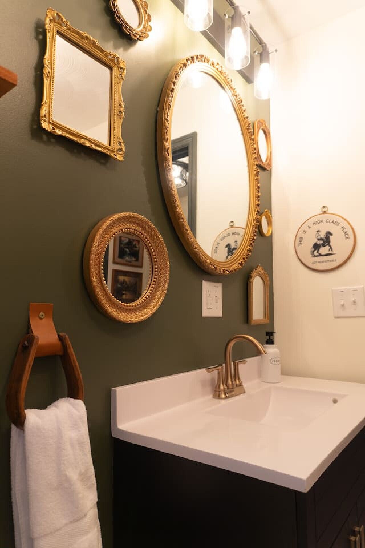 A bathroom with a white sink, gold-framed mirrors, and a towel rack.