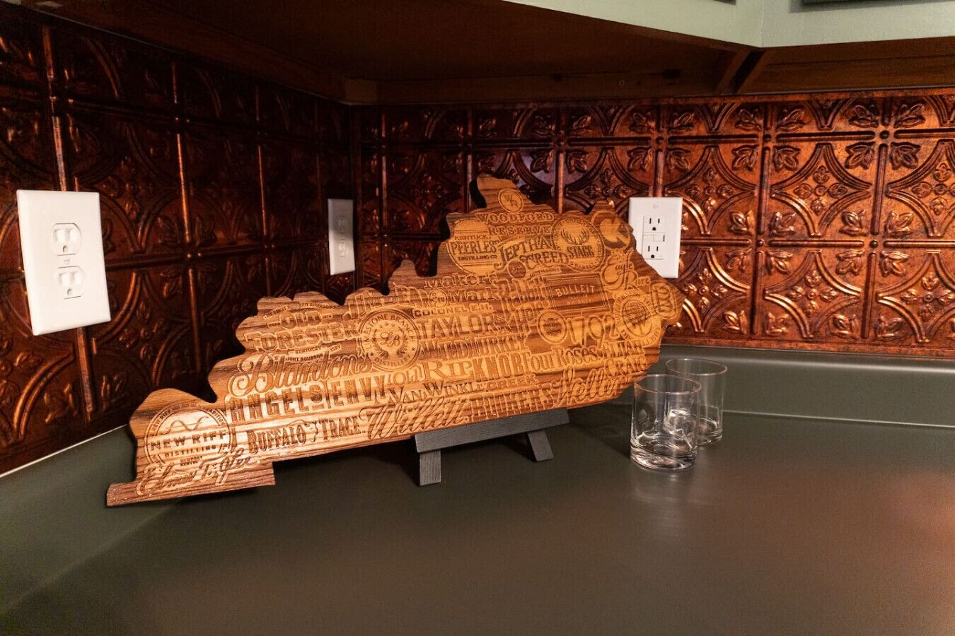 En træskulptur med præget tekst på et bord, sammen med et glas og en stikkontakt.