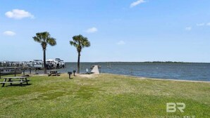 A waterfront park with picnic tables and benches, a small dock, and palm trees. - Tranquil 2-bedroom condo with Wolf bay views (Orange Beach)