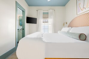 A bedroom with a large bed, a flat-screen TV mounted on the wall, a window with white curtains, and a checkered headboard. - Brand New, Chic 5 Bed Rental with Porch, Walkable (Charleston)