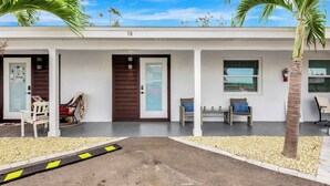 A two-story building with a white facade, numbered 18. There are two doors, a small porch area with seating, and a palm tree. - The Cozy Cove II 3 min to the beach (Bradenton)
