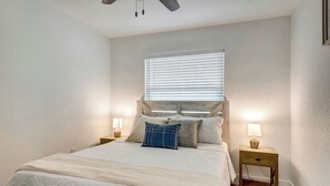 A bedroom with a bed, two bedside tables with lamps, a window with blinds, and a ceiling fan. - The Cozy Cove II 3 min to the beach (Bradenton)