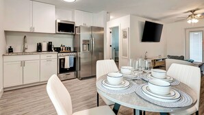 A modern kitchen with white cabinets, stainless steel appliances, and a dining area with white chairs and a round table set for four. - The Cozy Cove II 3 min to the beach (Bradenton)
