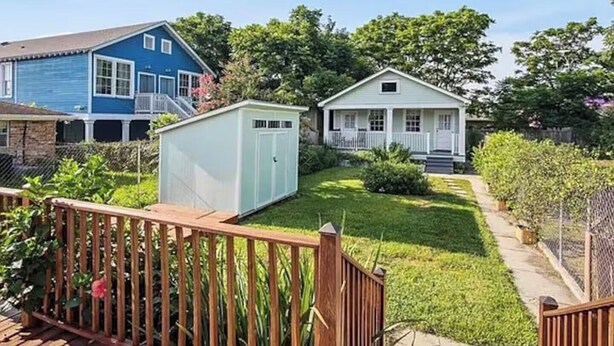 Una propiedad residencial con una casa azul, un cobertizo blanco y un porche delantero.