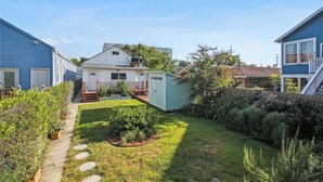 Un patio trasero residencial con un sendero, un cobertizo pequeño y una casa con porche.
