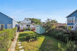 Een achtertuin met een pad, een tuinhuisje en een woning met een veranda.