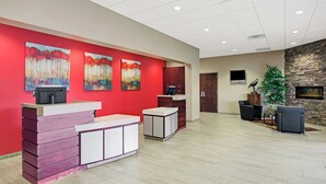 Un espace d’accueil avec un mur rouge, un comptoir d’accueil, un mur en pierre et un coin salon avec deux fauteuils.