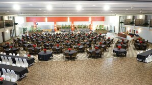 Une vaste salle d’événements intérieure, dotée de nombreuses tables et chaises rondes, d’une scène à l’avant et d’une mezzanine.