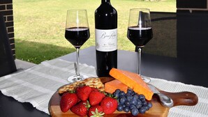 A table with a bottle of wine, two glasses, a wooden board with strawberries, blueberries, and cheese, and a view of a grassy area and buildings. - Two Williams Estate - Hunter Valley
4 Bedrooms, 2 Bathrooms, Pool Table (Kitchener)