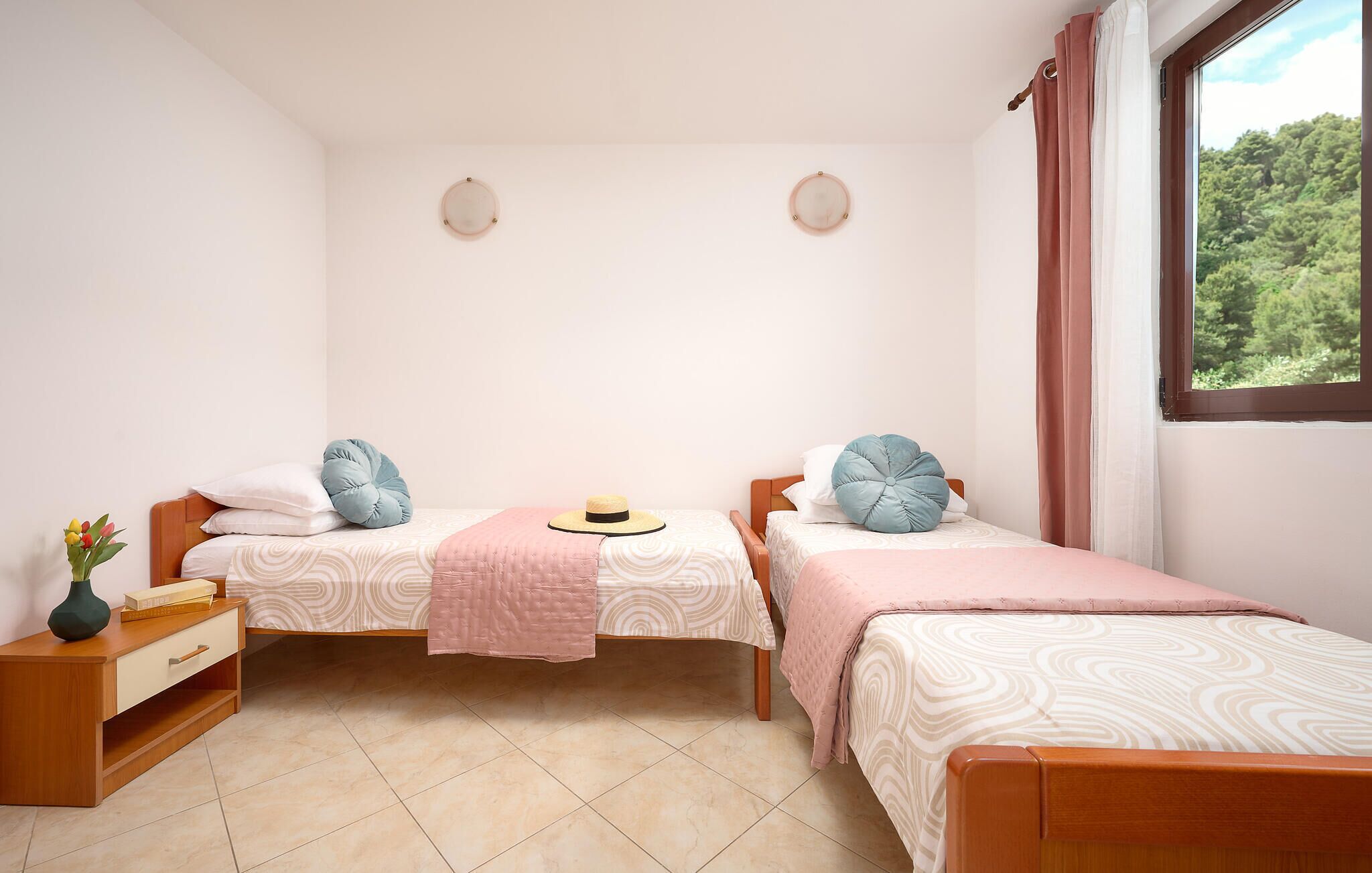 Camera da letto con due letti singoli, un comodino, una tenda e vista sul verde.