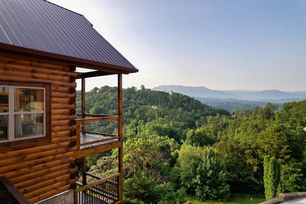 A log cabin with a balcony overlooking a forested valley.