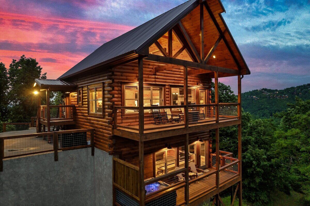 A multi-level log cabin with a balcony, a hot tub, and a scenic view of the forest.
