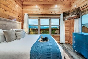 A wooden cabin room with a bed, a dresser, and a large window offering a view of the mountains. - A Spectacular View! *Hot Tub*Games*Pool*Dollywood! (Sevierville)