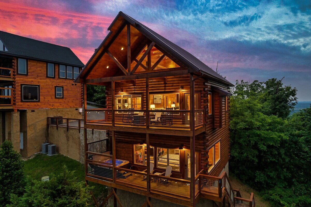 Une cabane en rondins à plusieurs niveaux, dotée d’un balcon, d’un jacuzzi et offrant une vue sur la forêt environnante.
