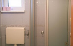 A bathroom with a toilet, a shower with a glass door, and a window with a shelf holding two pink towels. - Awesome apartment in Jezera with house sea view (Jezera)