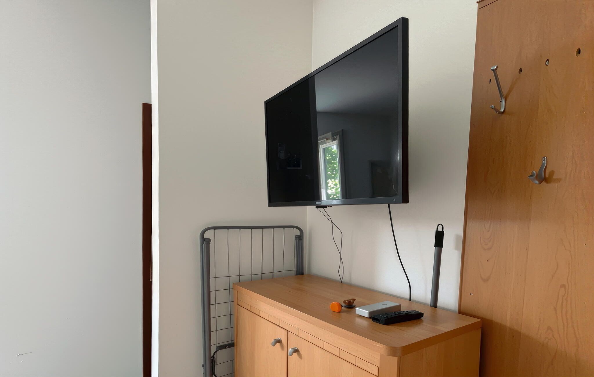 A room with a mounted flat-screen TV, a wooden cabinet with drawers, a radiator, and a wooden door.