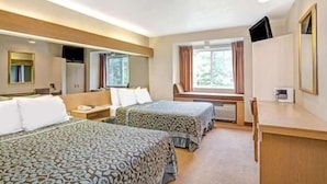 Ett hotellrum med två sängar, ett skrivbord, en stol, en TV och ett fönster med gardiner.