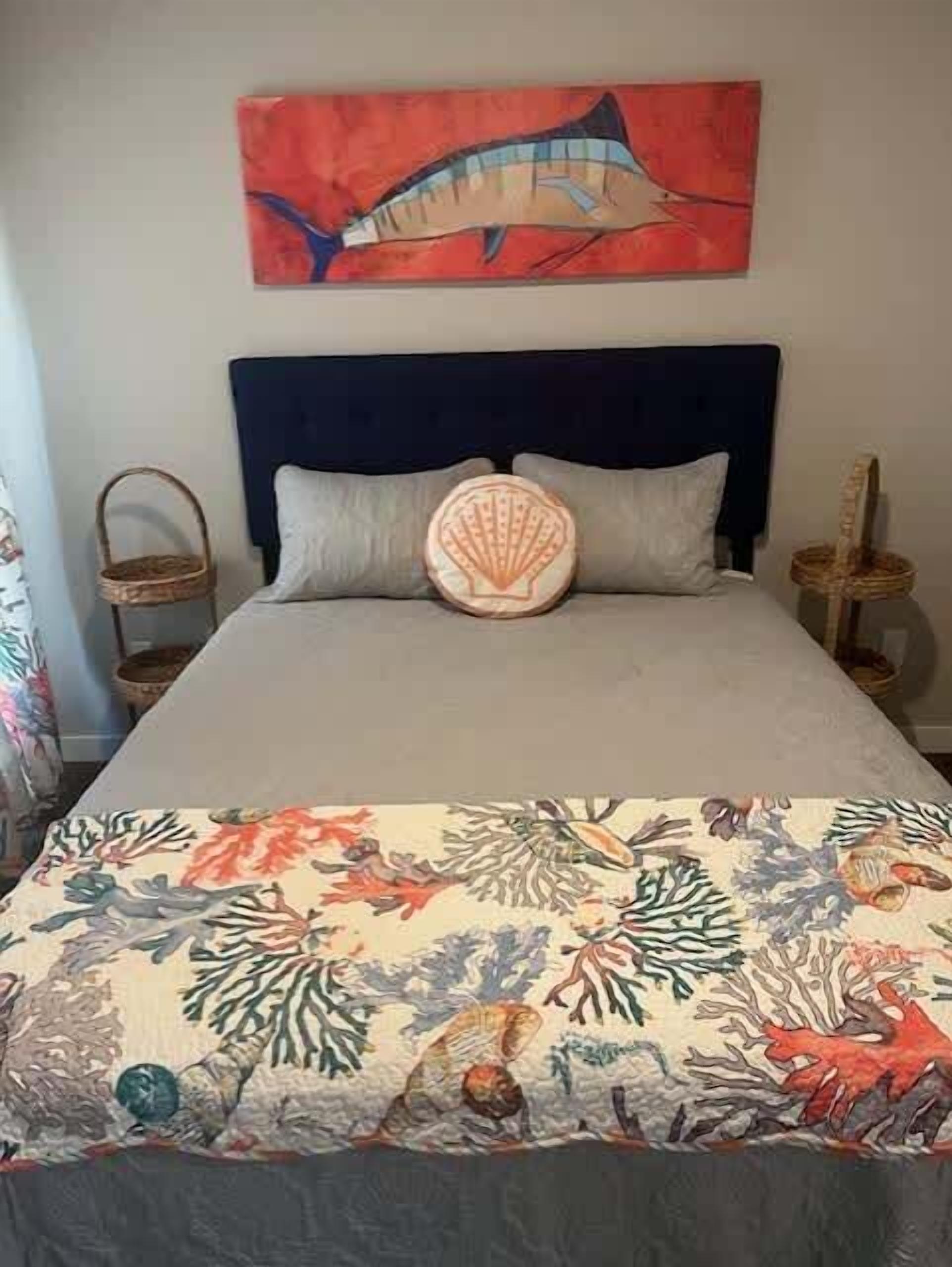 A bed with a blue headboard, two pillows, and a colorful bedspread with marine life.