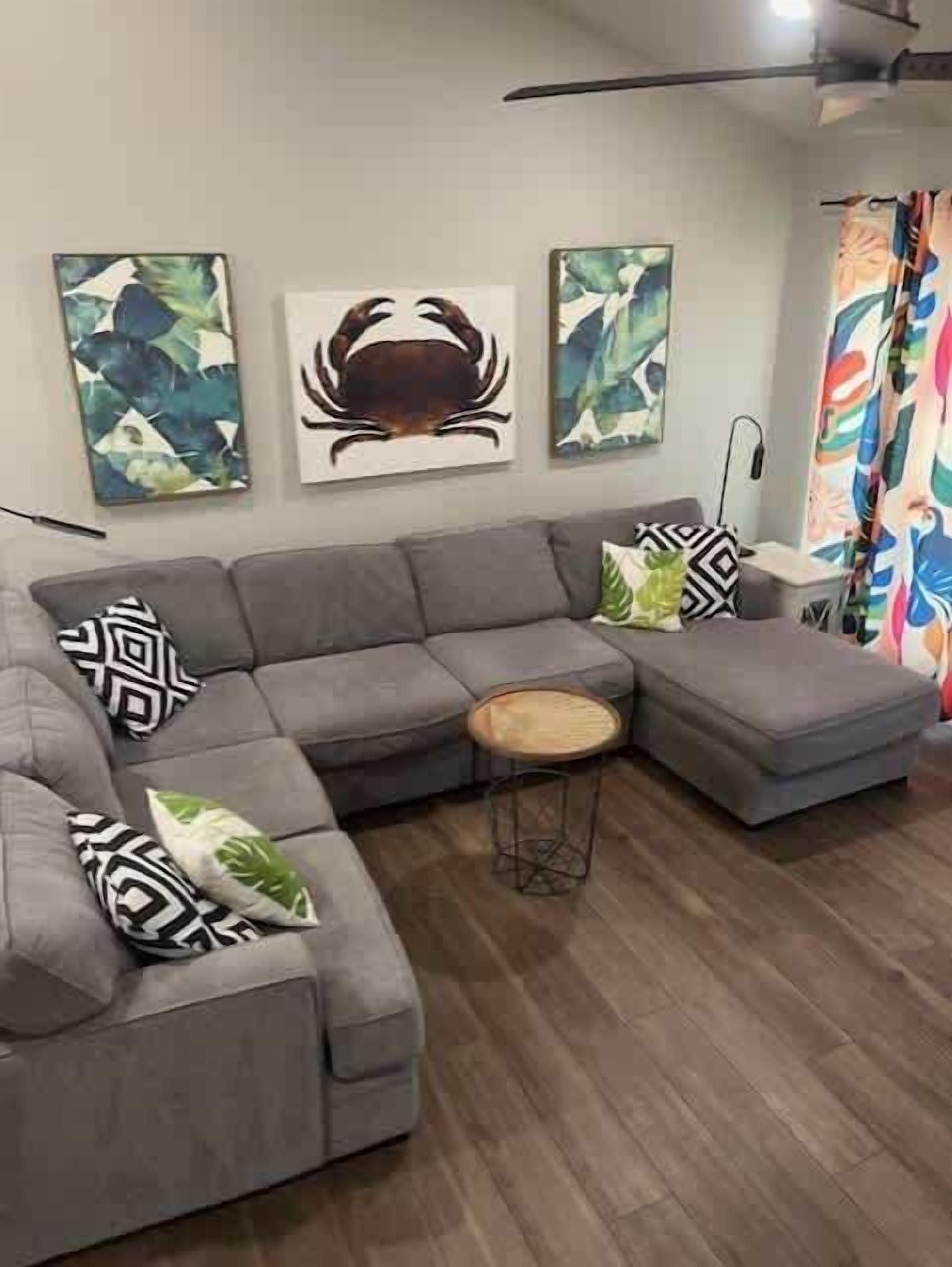 A modern living room with a grey sectional sofa, a round wooden side table, and abstract wall art.