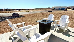 Eine Terrasse mit Adirondack-Stühlen und einem quadratischen Tisch, vor einer Kulisse aus blauem Himmel und weiter Ferne.