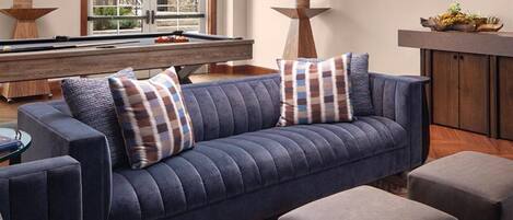 Una sala de estar moderna con un sofá azul, dos otomanas a juego, una mesa de billar y un aparador de madera.