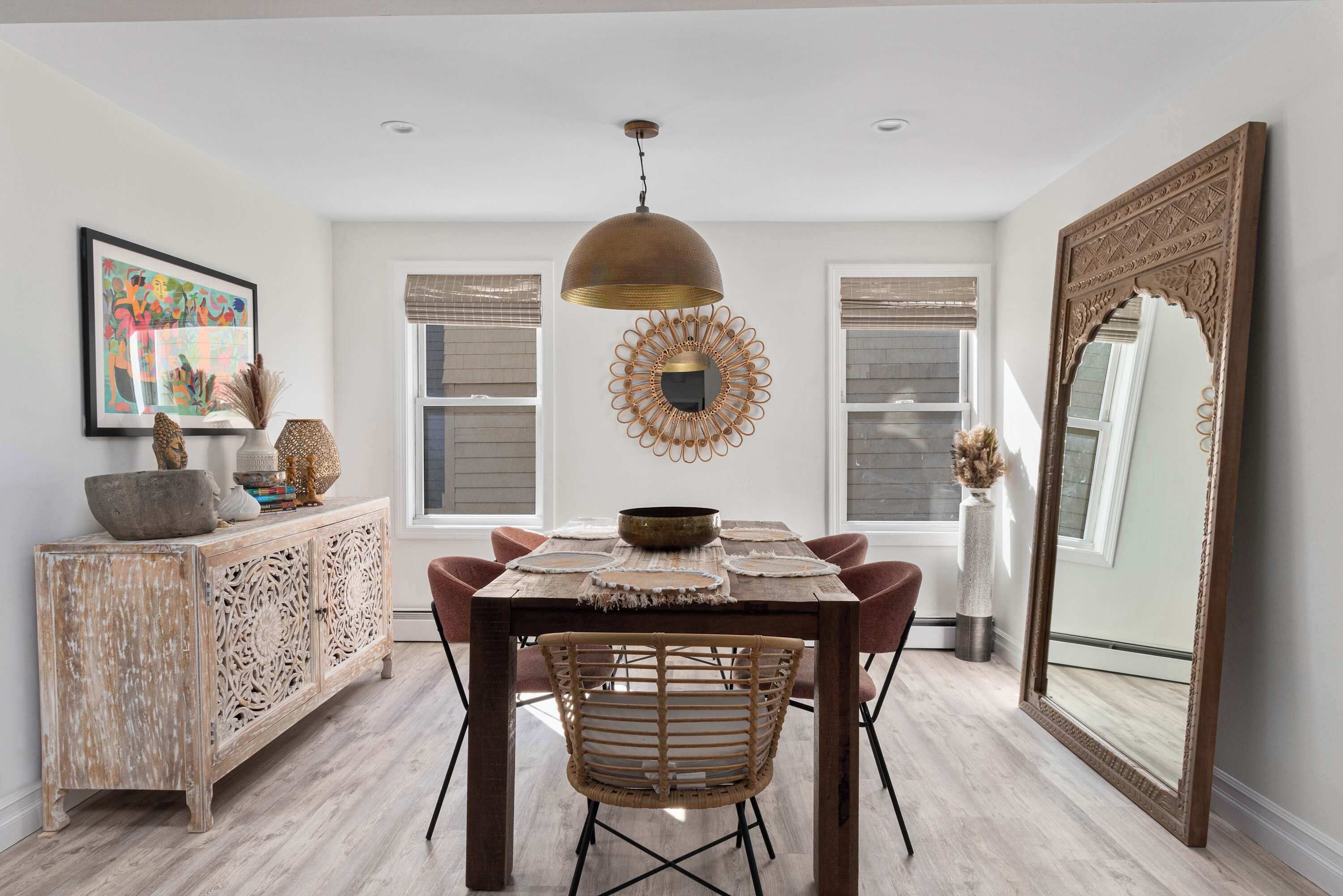 Un coin repas comprenant une table en bois, des chaises, un luminaire suspendu, un miroir décoratif et un meuble au design rustique.