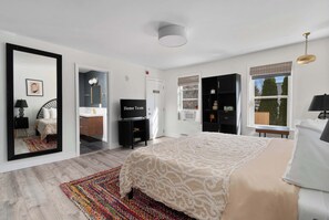 A bedroom with a large bed, a TV, a wardrobe, and a mirror.