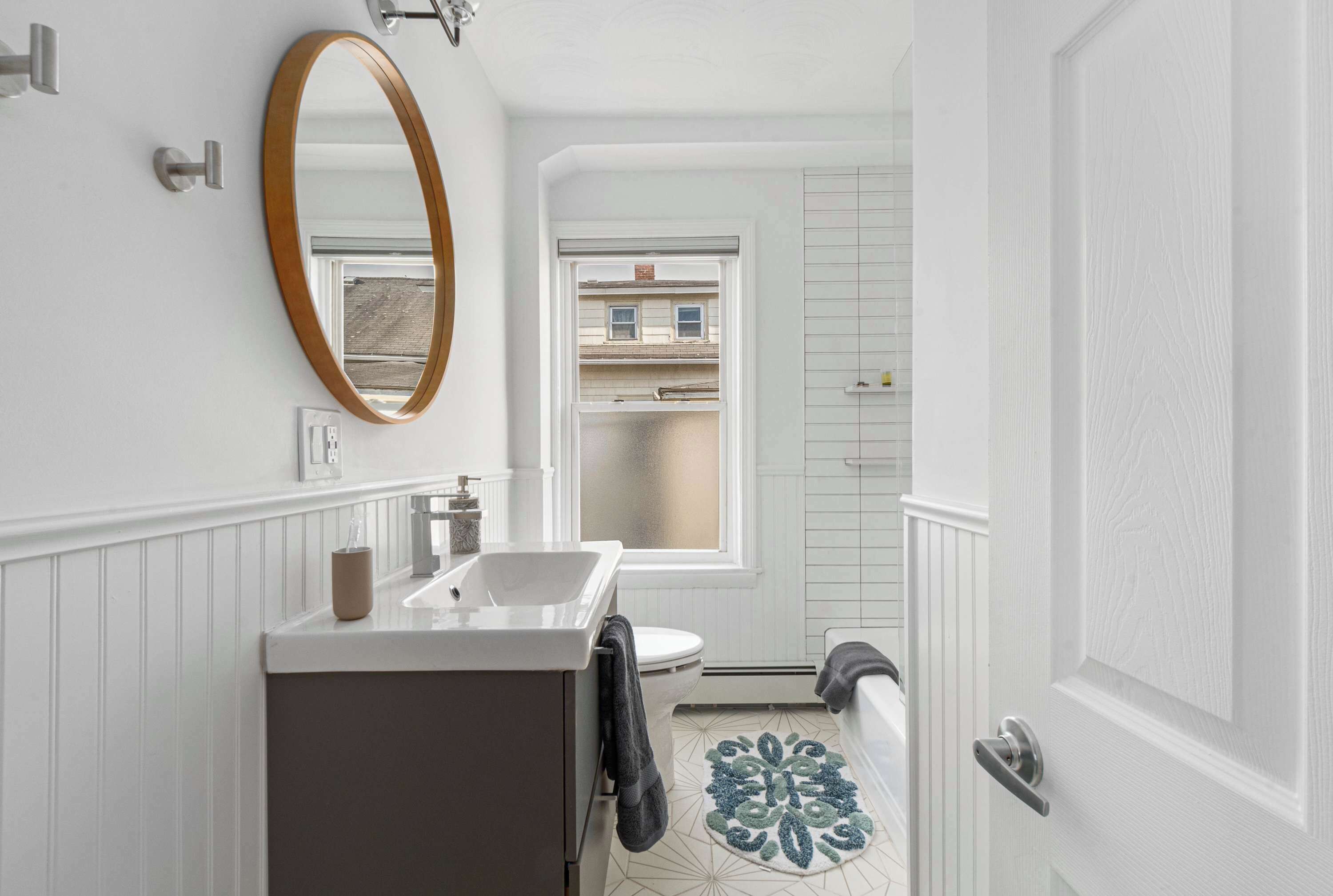 Un baño con tocador blanco, espejo, inodoro, bañera y ventana.