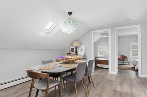 A modern dining area with a wooden table, grey chairs, and a unique glass chandelier. - Downtown Warren Top Floor Loft 3BR: Spa | Walkable (Warren)