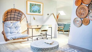 Una sala moderna con un sillón colgante, una mesita redonda, un escritorio con silla y una pared decorada con cestas tejidas.